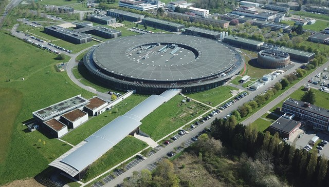 Vue aérienne du synchrotron Soleil. Au fond un grand bâtiment circulaire. Deux bâtiments allongés en sortent